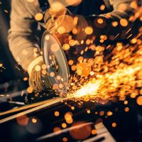 Metal worker cutting a metal objects with circular saw in small workshop.